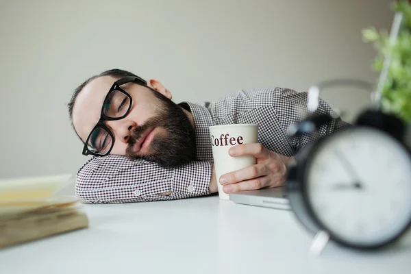 Homme dort dans le bureau sur la table sur un ordinateur portable avec du café à la main — Photo