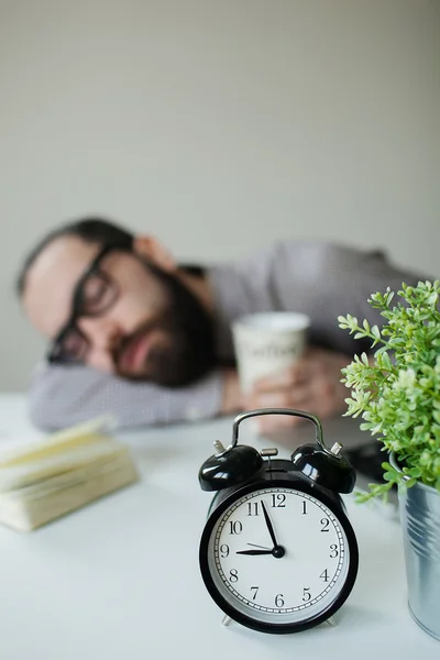 Člověk spí v kanceláři na stole za laptop s kávou v ruce — Stock fotografie