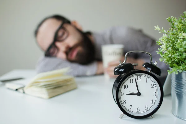 Man sleeps in office on table over laptop with coffee in hand — Stock Photo, Image