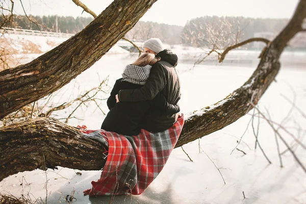 Hipster paar zittend op boom over bevroren meer — Stockfoto