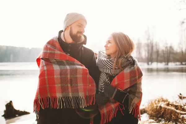 Couple looking each other near winter lake under plaid — Stock Photo, Image