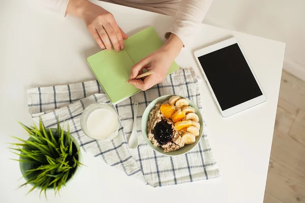 Donna che prende appunti in blocco note con cibo sano in tavola — Foto Stock