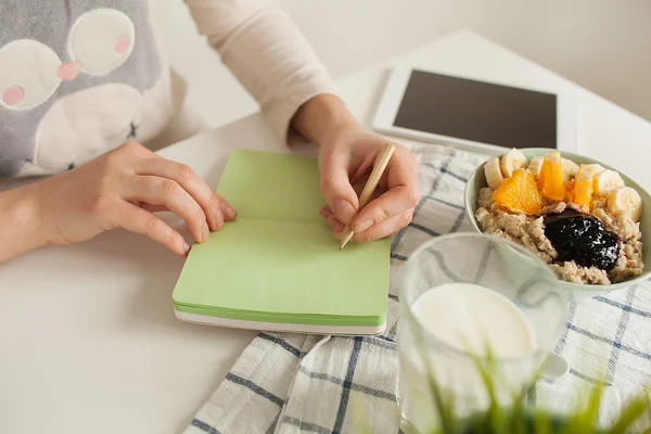 Mujer haciendo notas en bloc de notas con comida saludable en la mesa — Foto de Stock