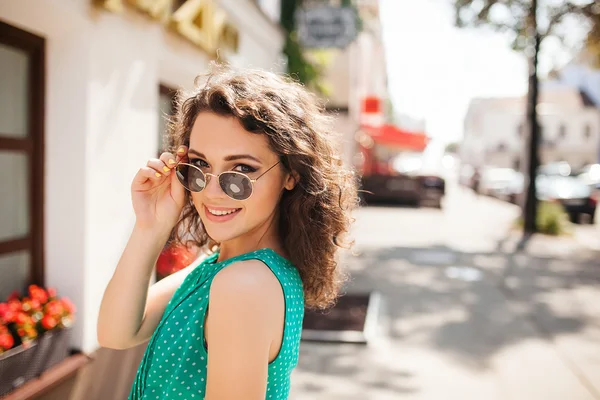 Frau mit runder Sonnenbrille lächelt in Stadtstraße über die Schulter — Stockfoto