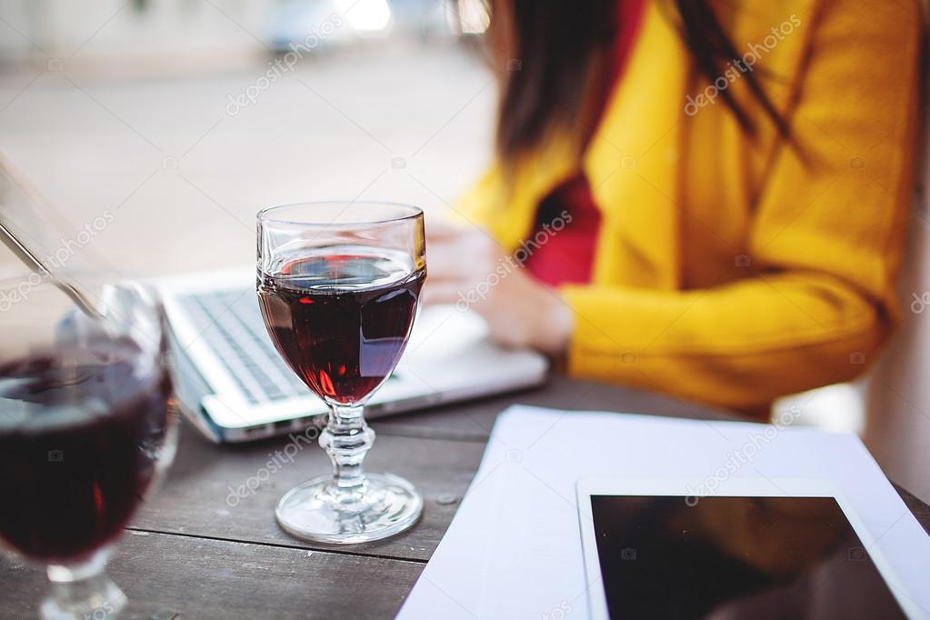 Woman with red wine tablet and laptop in street cafe