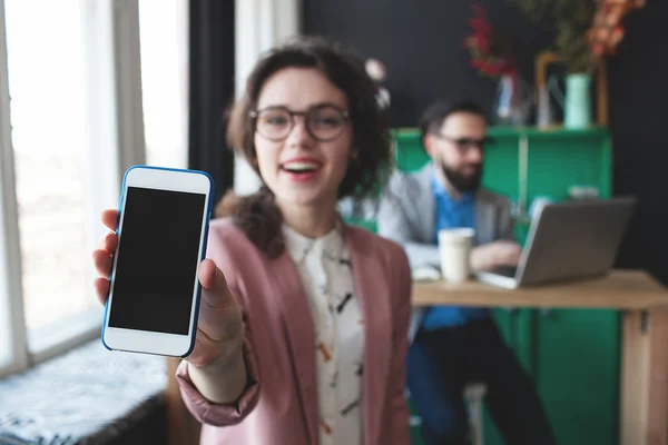 Woman in glasses showing smartphone and businessman working on b — Stock Photo, Image