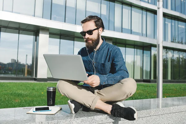 Businessman in sunglasses with laptop outdoors in front of offic — Stock Photo, Image