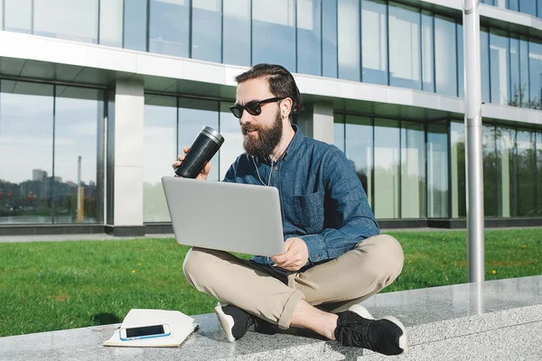 Empresário em óculos de sol com laptop bebendo café ao ar livre — Fotografia de Stock