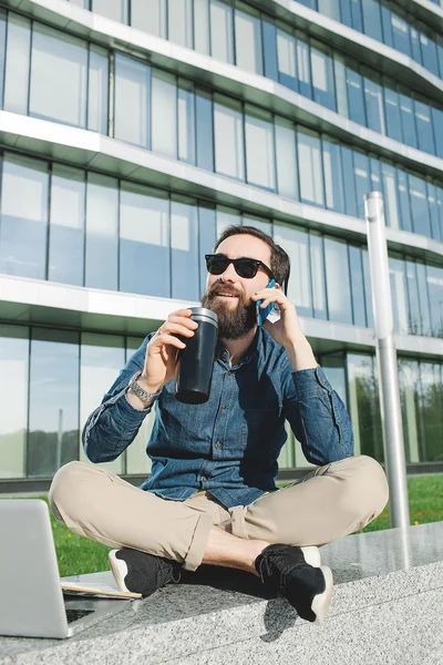 Jovem empresário em óculos de sol com laptop coffe falando telefone — Fotografia de Stock