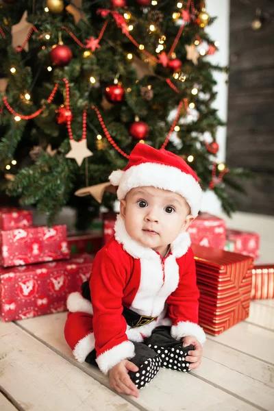 Baby i santa dress med gaver nær juletreet – stockfoto