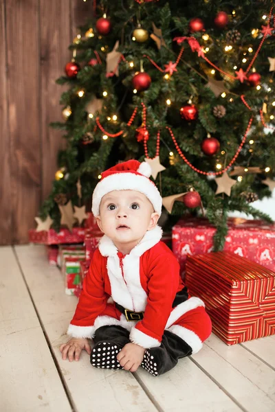 Bébé en costume de Père Noël avec des cadeaux près de l'arbre de Noël — Photo