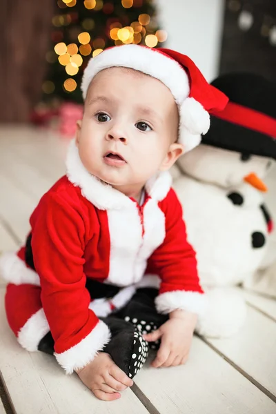 Dítě v obleku santa na podlahu vedle vánoční strom — Stock fotografie