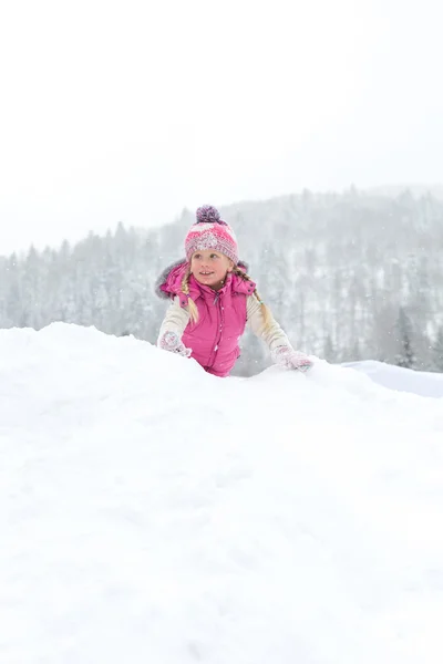 Lille pige lykkeligt leger i sneen - Stock-foto