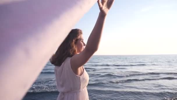 Hermosa mujer sosteniendo tela ligera en la playa y disfrutar de la puesta de sol — Vídeos de Stock