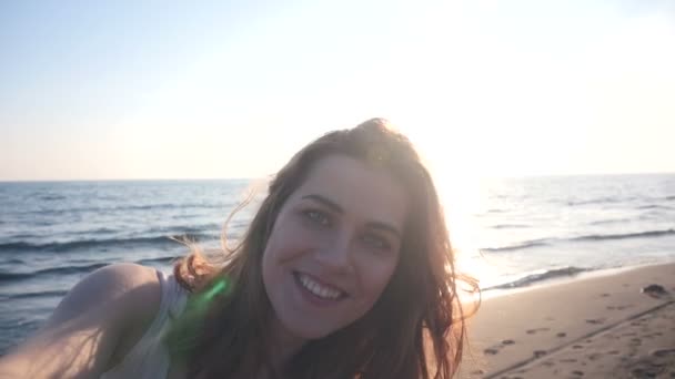 Красива жінка бере селфі, використовуючи телефон на пляжі на заході сонця посміхаючись і кружляючи насолоджуючись природою і способом життя — стокове відео