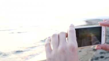 güzel genç kadın bir smartphone kullanarak sahilde Günbatımı Fotoğraf çekimi