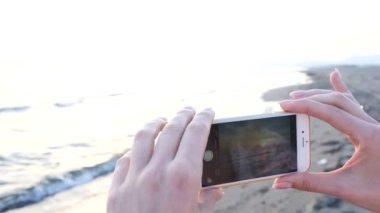 güzel genç kadın bir smartphone kullanarak sahilde Günbatımı Fotoğraf çekimi