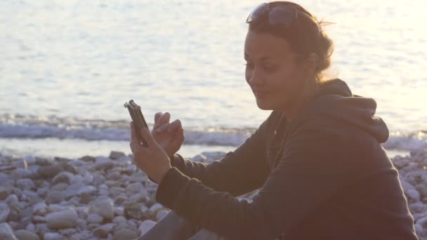 Aantrekkelijke vrouw is het gebruik van smartphone bij zonsondergang — Stockvideo