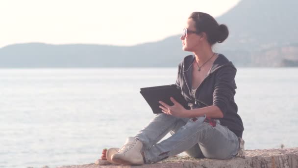 Kobieta za pomocą tabletu na plaży podczas zachodu słońca — Wideo stockowe