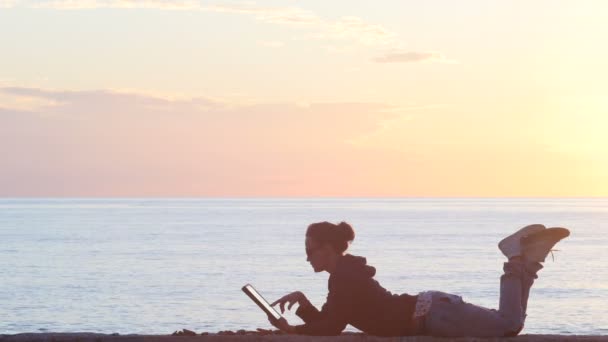Γυναίκα χρησιμοποιώντας ένα tablet στην παραλία κατά τη διάρκεια του ηλιοβασιλέματος — Αρχείο Βίντεο