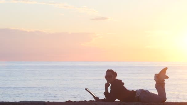 Mujer usando una tableta en la playa al atardecer — Vídeos de Stock