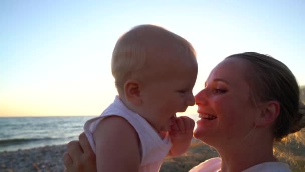 Mama, rozpieszczanie dziecko siedzi na plaży o zachodzie słońca — Wideo stockowe
