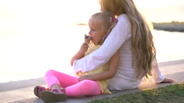 Nettes kleines Mädchen, das Eis isst, während es auf der Promenade in den Armen seiner Mutter sitzt — Stockvideo