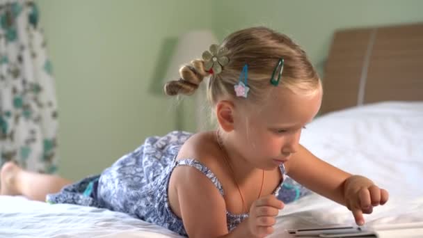 Pequena menina bonito joga um jogo no tablet — Vídeo de Stock