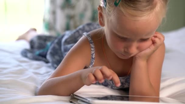 Pequena menina bonito joga um jogo no tablet — Vídeo de Stock