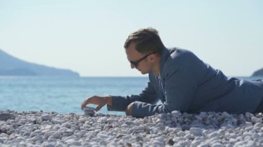 Ceketli bir adam kumsalda yatarken bir Zen piramidi inşa eder.