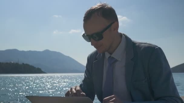 Freelancer businessman working remotely on laptop at the beach — Stock Video