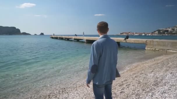 Un hombre con una chaqueta con un portátil está en la playa con los brazos extendidos a los lados — Vídeos de Stock