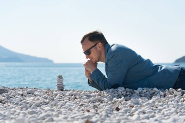 Ceketli bir adam kumsalda yatar ve zen piramidine bakar.