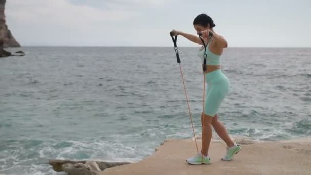 Αθλητική τακτοποίηση γυναίκα κάνει σωματική άσκηση γυμναστικής στην παραλία, χρησιμοποιώντας expander γυμναστικής για τα χέρια άσκηση. — Αρχείο Βίντεο
