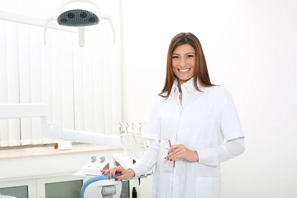 Girl dentist near the dental chair holding safety glasses — Stock Photo, Image