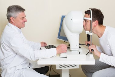 Man having his eyes examined by an eye elderly doctor. clipart