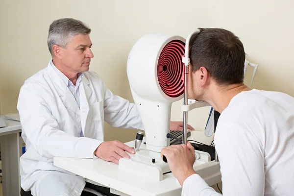 Gözleri bir gözü yaşlı doktor tarafından muayene olan adam.