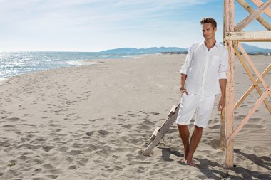 Sahilde poz Beyaz giysili genç çekici adam 