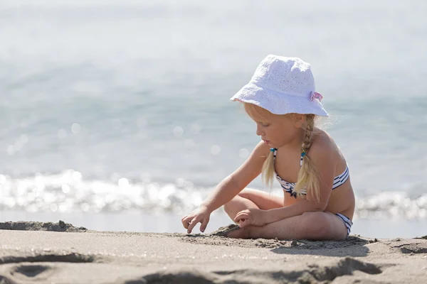 Kleines Mädchen sitzt am Strand. — Stockfoto