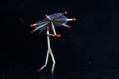 Yağmurda kibrit çöpü şemsiyeli bir adam. Yağmur konsepti. Kibrit çöpü sanat fotoğrafçılığı karakteri oluşturmak için kibrit çöpleri kullanır.