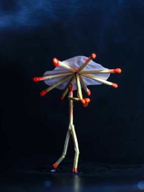 Yağmurda kibrit çöpü şemsiyeli bir adam. Yağmur konsepti. Kibrit çöpü sanat fotoğrafçılığı karakteri oluşturmak için kibrit çöpleri kullanır.