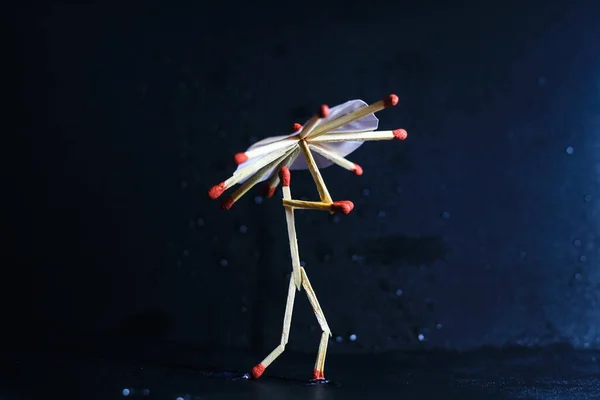 A matchstick man with a matchstick umbrella in the rain. Raining concept. Matchstick art photography used matchsticks to create the character.