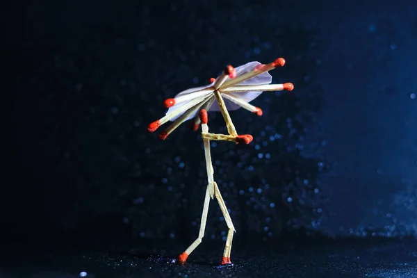 A matchstick man with a matchstick umbrella in the rain. Raining concept. Matchstick art photography used matchsticks to create the character.