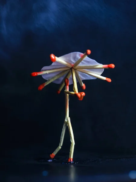A matchstick man with a matchstick umbrella in the rain. Raining concept. Matchstick art photography used matchsticks to create the character.