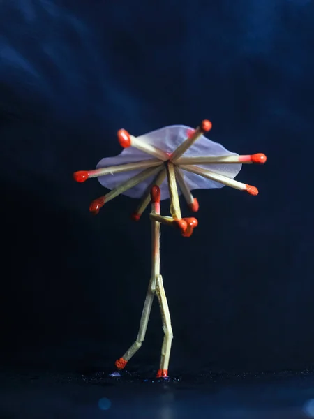 A matchstick man with a matchstick umbrella in the rain. Raining concept. Matchstick art photography used matchsticks to create the character.