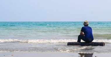 Güneş doğarken kumsalda oturan genç bir adamın dikiz aynasındaki cennet manzarası manzarası ve mavi deniz dalgalarını seyrederken. Deniz dalgalarının tadını çıkaran yalnız bir adam.