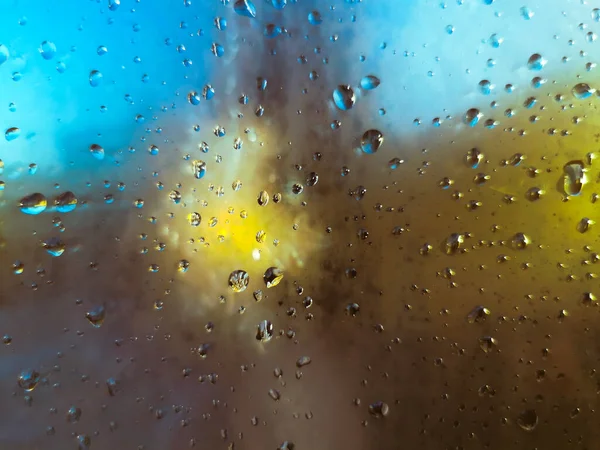 雨は抽象的な黄色と青の背景を持つウィンドウに落ちます — ストック写真