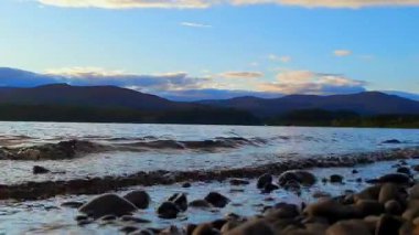 Loch Insh Gölü 'nün Zaman Kaynağı İskoç İskoçya' sının kalbinde yer alan çarpıcı bir zaman dilimi videosu. Güneş etrafındaki dağların ardında batarken göl boyunca hafif dalgalar hareket eder. Mavi ve altın renkleri ile gökyüzünü boyarlar.. 
