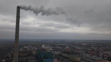 Romanya 'nın Bükreş kentindeki bir termik santral bacasının hava aracı görüntüleri. Video, bulutlu bir kış gökyüzü altında kentsel alanın üzerine duman salan bir endüstriyel baca yığınını gösteriyor..