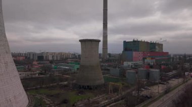 Romanya 'nın Bükreş kentinde bir termik santral soğutma kulesi ve bacanın hava aracı görüntüleri. Yükselen çekim, serinleme yapısı, baca ve etrafındaki sanayi binalarını bulutlu bir kış gökyüzü altında ortaya çıkarıyor..
